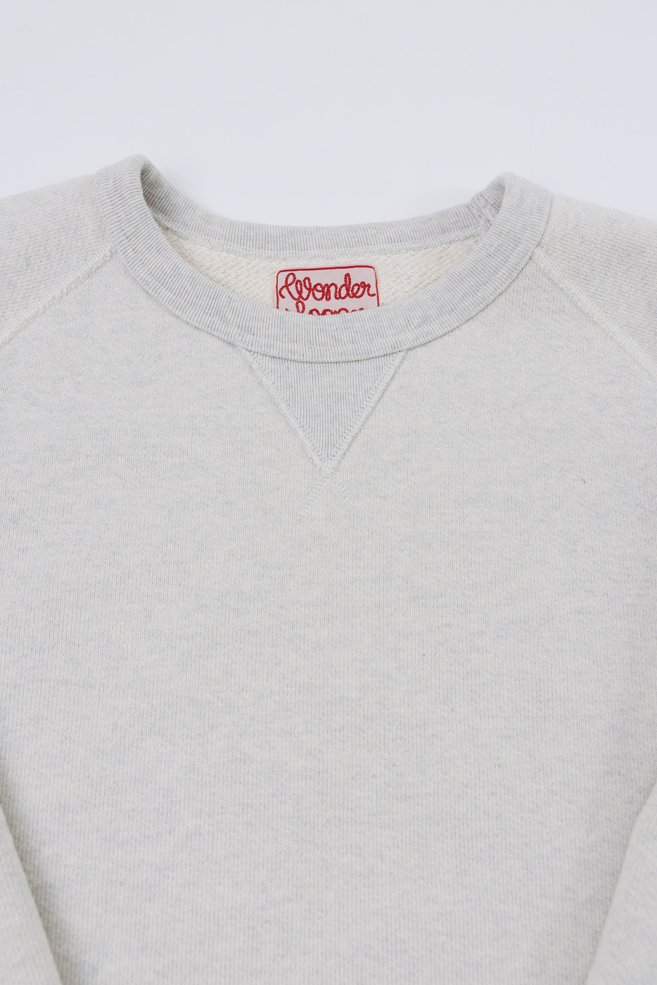 Close-up front view of a light grey sweatshirt collar and red Wonder brand neck tag.