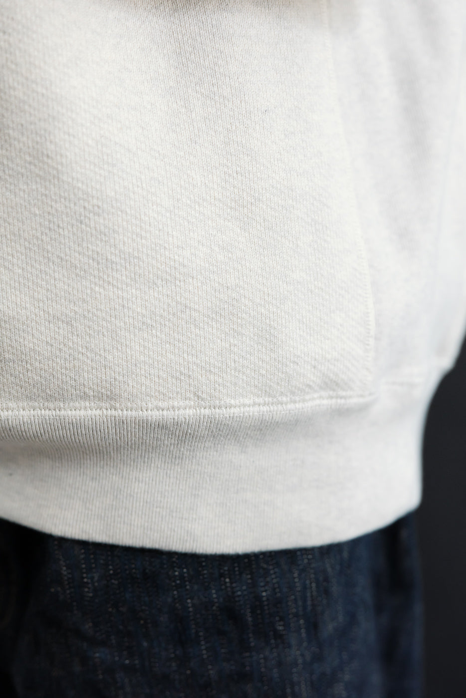 Close-up of the front bottom hem and ribbed waistband of a light grey sweatshirt.