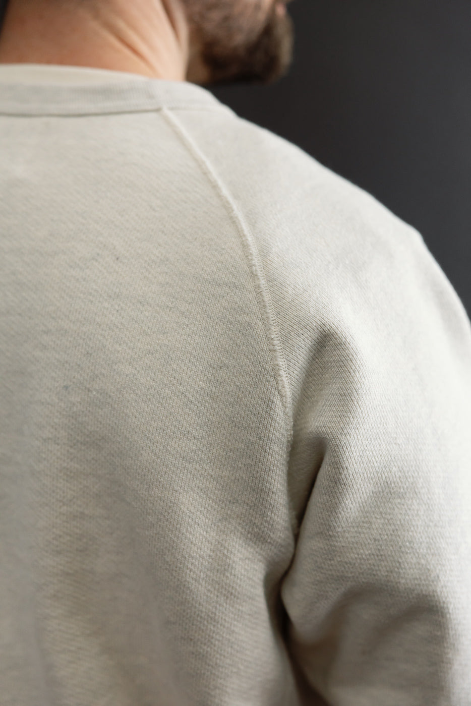 Close-up of the back shoulder and raglan sleeve of a cream-colored crewneck sweatshirt.