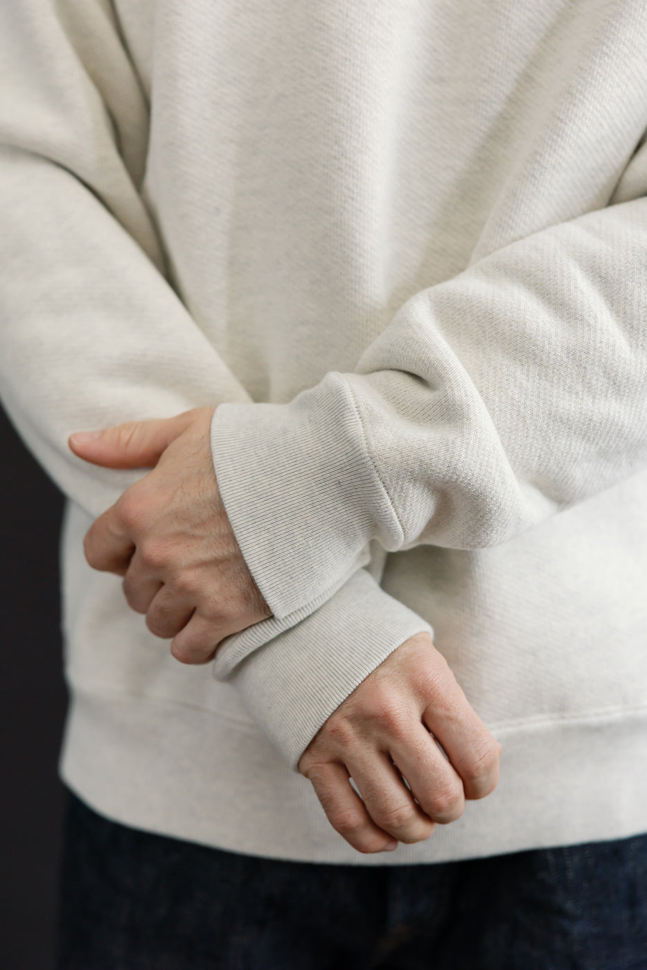 Close-up of the ribbed cuff and sleeve detail on a cream sweatshirt worn by a male model.