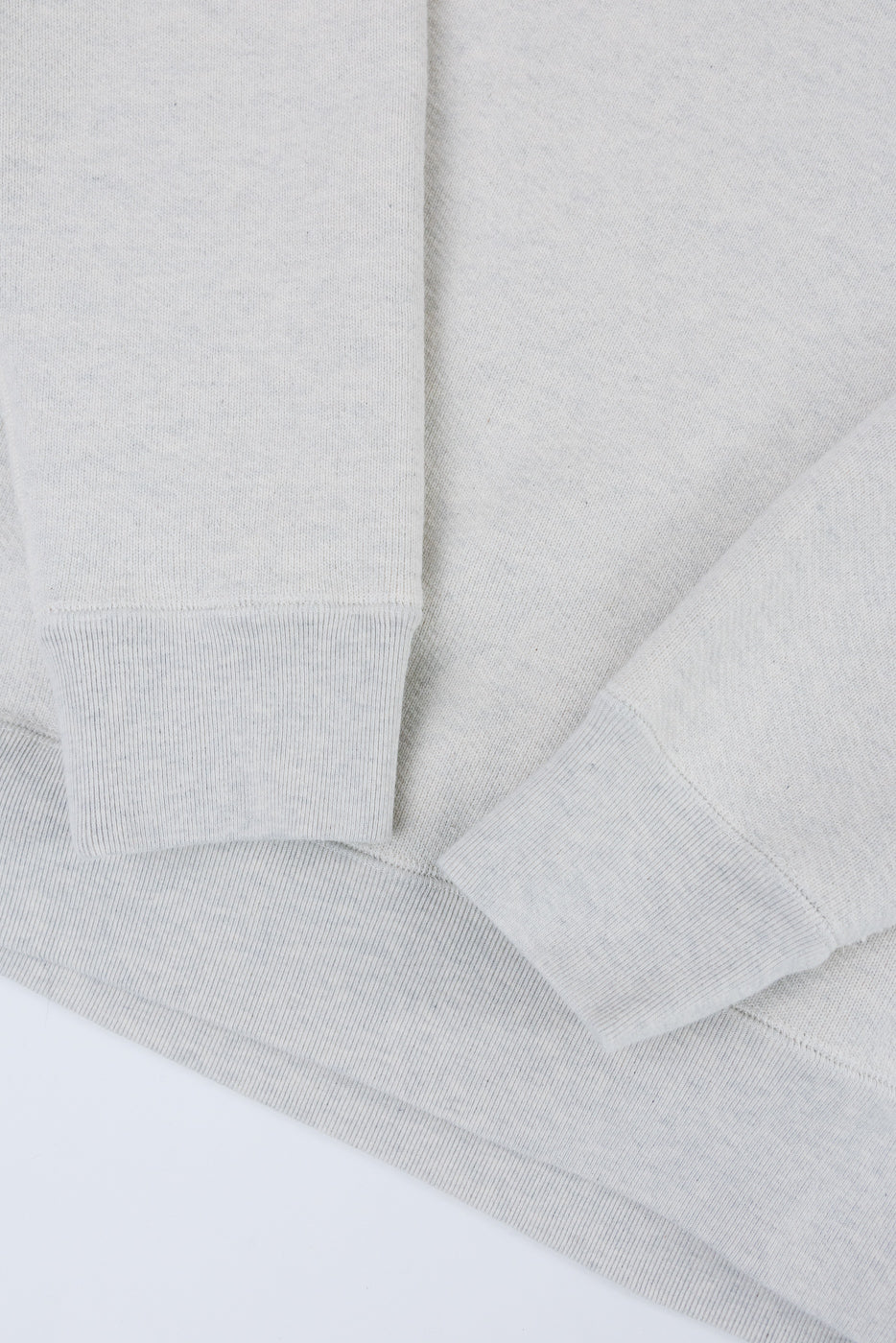 Close-up of the ribbed cuffs and hem on a light grey sweatshirt flat lay.