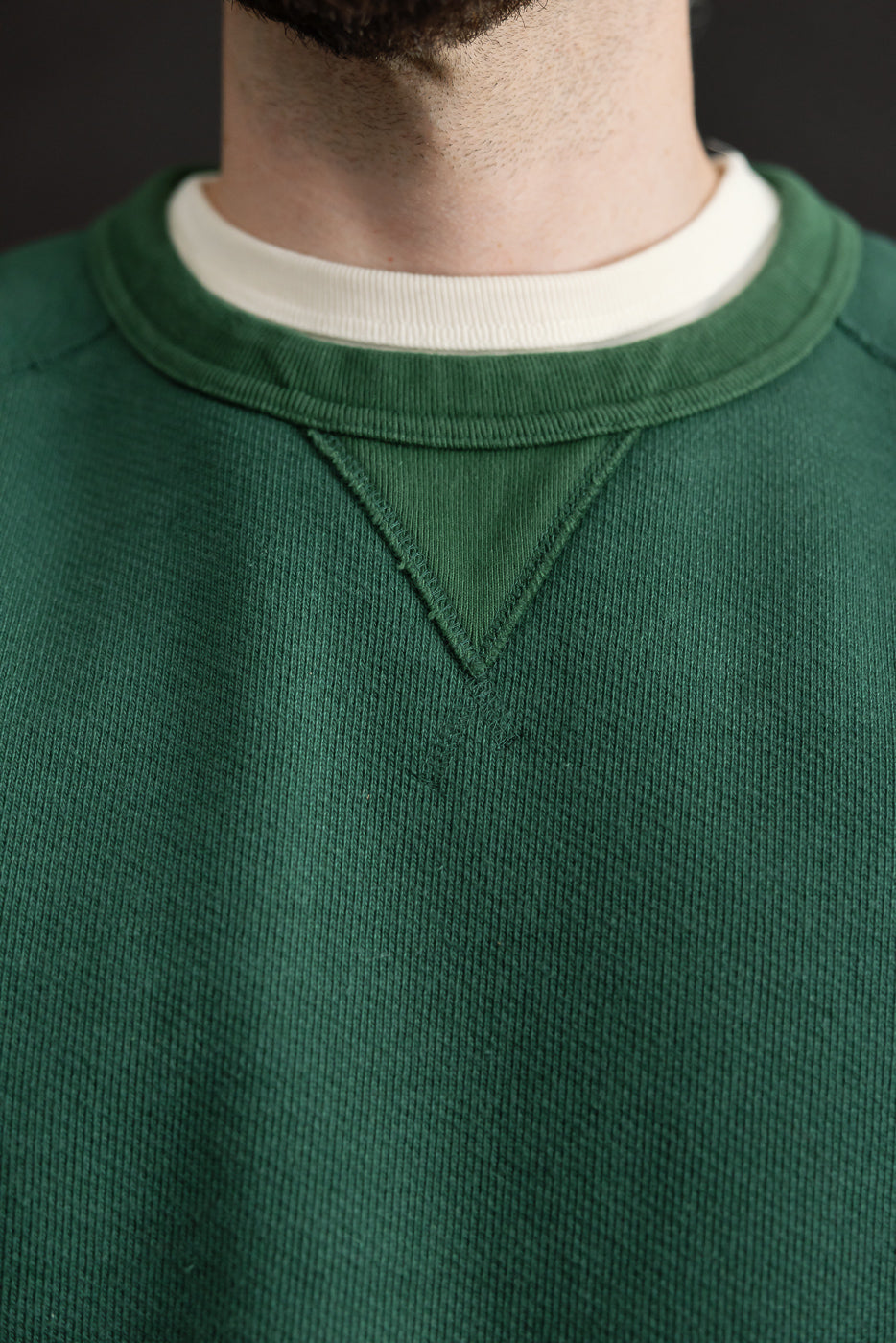 Close-up of the front neckline of a male model's green crewneck sweatshirt showing the ribbed collar.