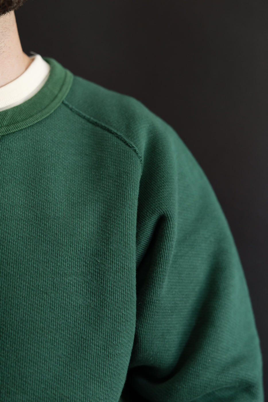 Close-up of the front right shoulder and sleeve of a green crewneck sweatshirt.