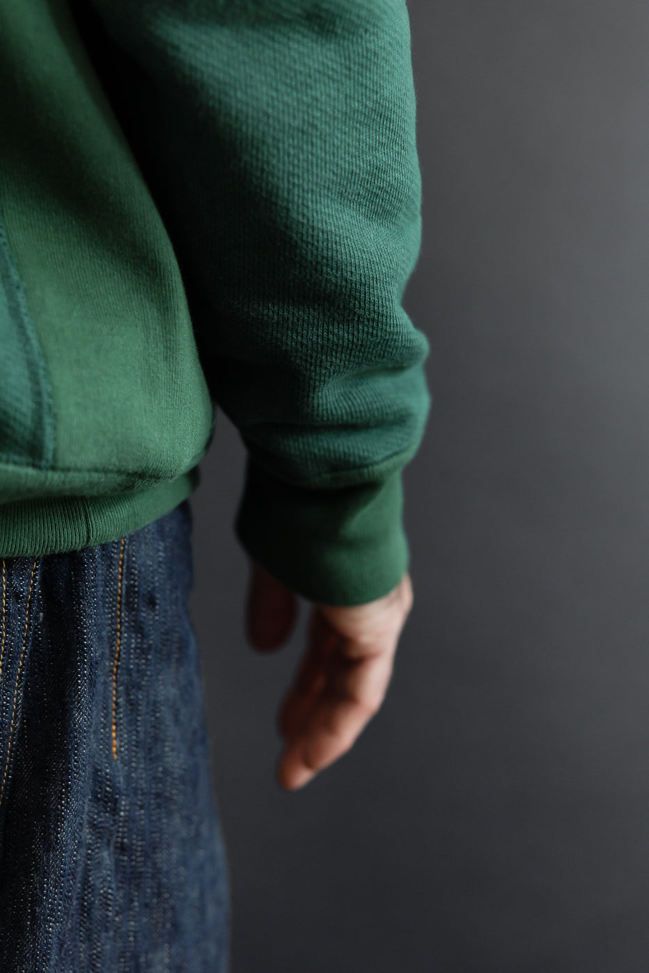 Close-up side view of a green fleece hoodie sleeve and ribbed cuff paired with dark denim jeans.