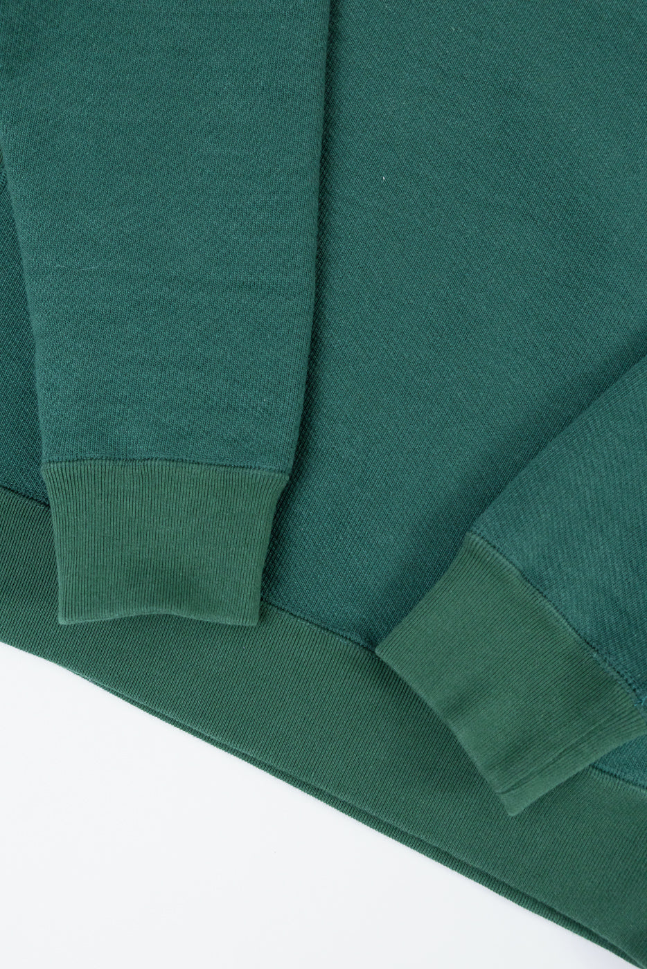 Close-up of a green sweatshirt's ribbed cuff and bottom hem on the front side.