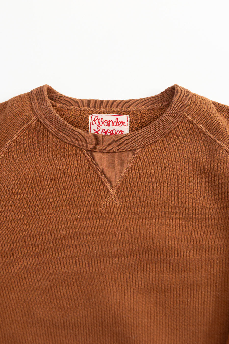 Close-up of Wonder Looper pullover crewneck front collar, rust French terry fabric, tag detail.