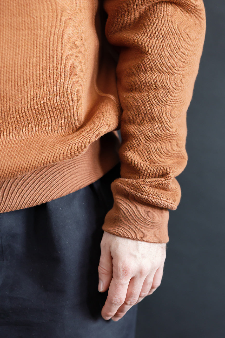 Close-up of male model's right side wearing rust Wonder Looper pullover crewneck, showing sleeve and hem texture. Model is 5'9