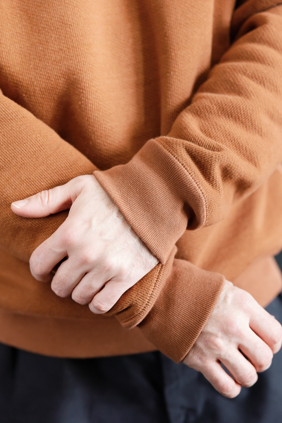 Close-up of male model’s hands and sleeves in rust Wonder Looper pullover crewneck, showing French terry fabric and ribbed cuffs, Dant contemporary casualwear.