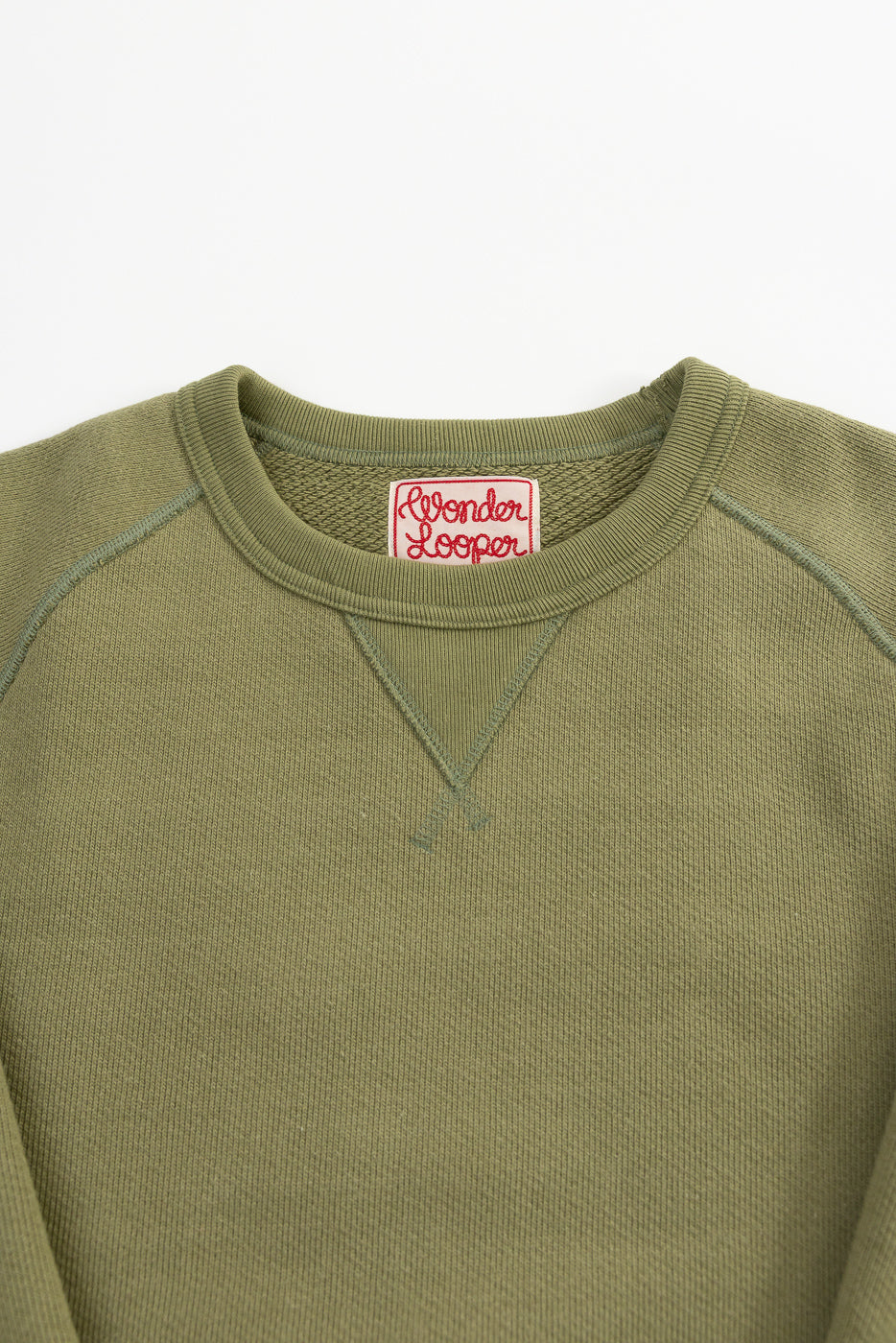Close-up of Wonder Looper sage green pullover crewneck front, showing ribbed collar, V-stitch, tag, and heavyweight French terry texture.