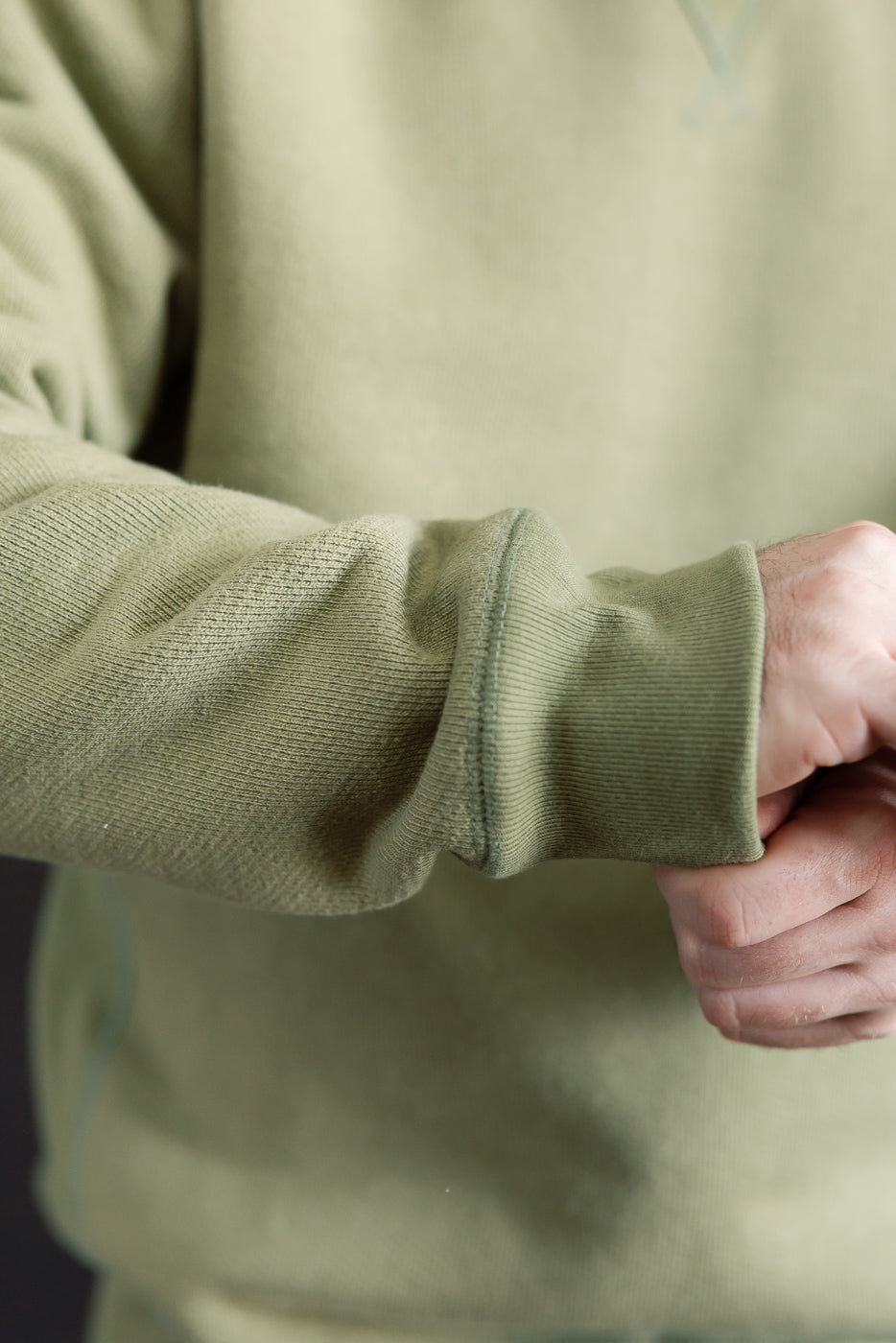 Close-up of male model's arm in sage green Wonder Looper pullover crewneck, showcasing French terry sleeve texture and ribbed cuff, Dant contemporary casual style.