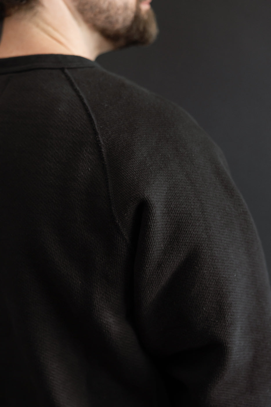 Close-up of the back and shoulder of a black textured sweatshirt on a male model.