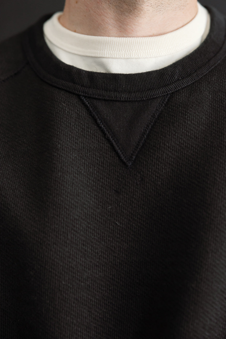 Close-up front view of a black sweatshirt neckline on a male model, 5'9
