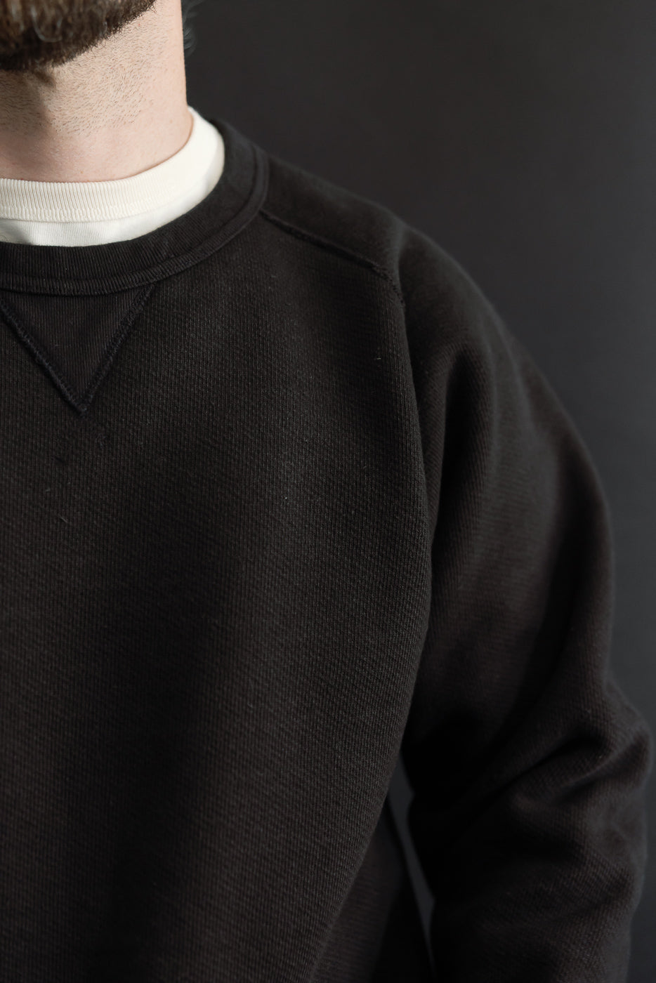 Close-up of the front and left shoulder of a dark brown textured crewneck sweatshirt.