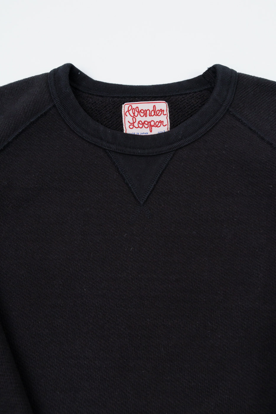Close-up of the front neckline of a black sweatshirt featuring a Wonder Looper tag.