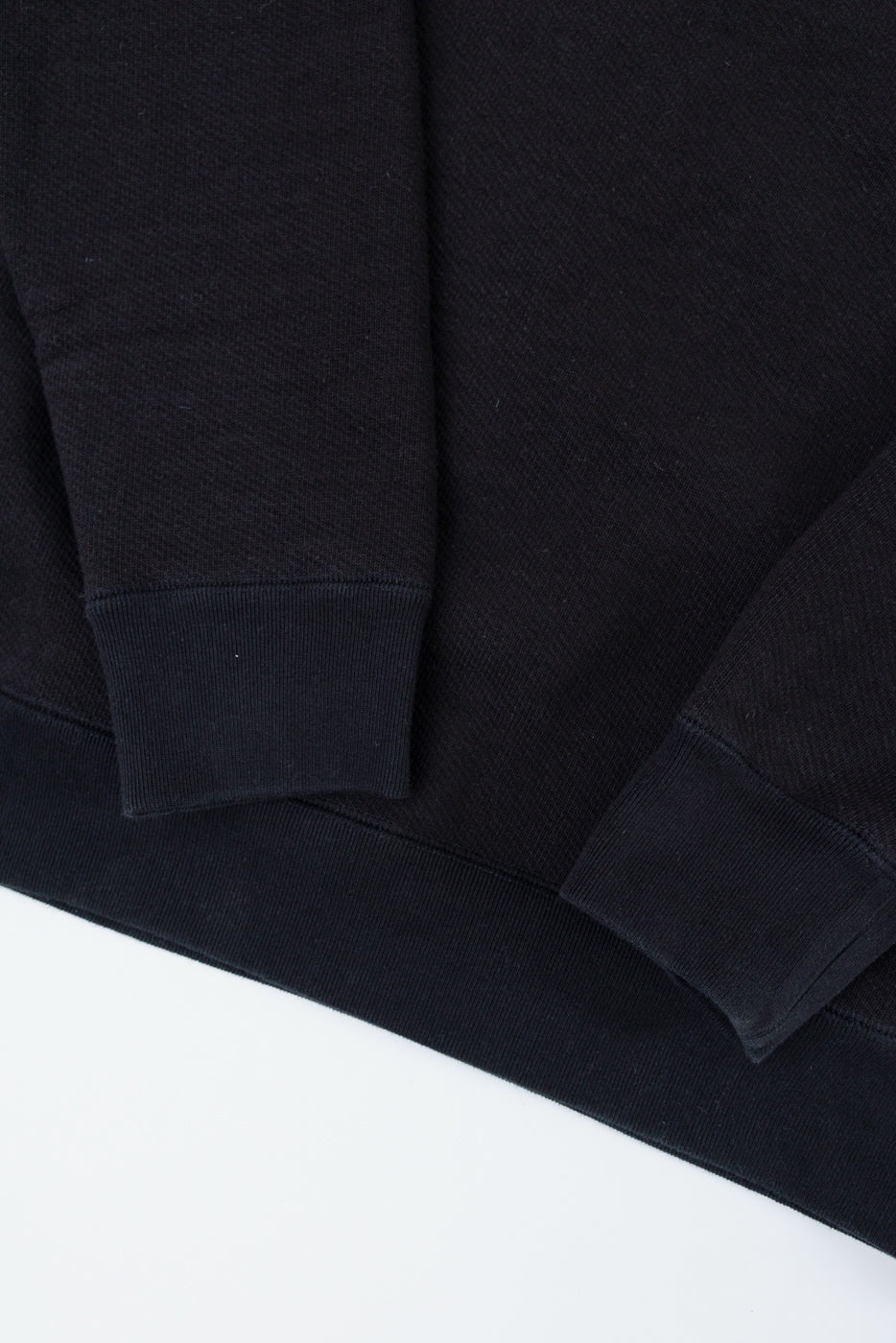 Close-up of the ribbed cuffs and hem of a black sweatshirt fabric.