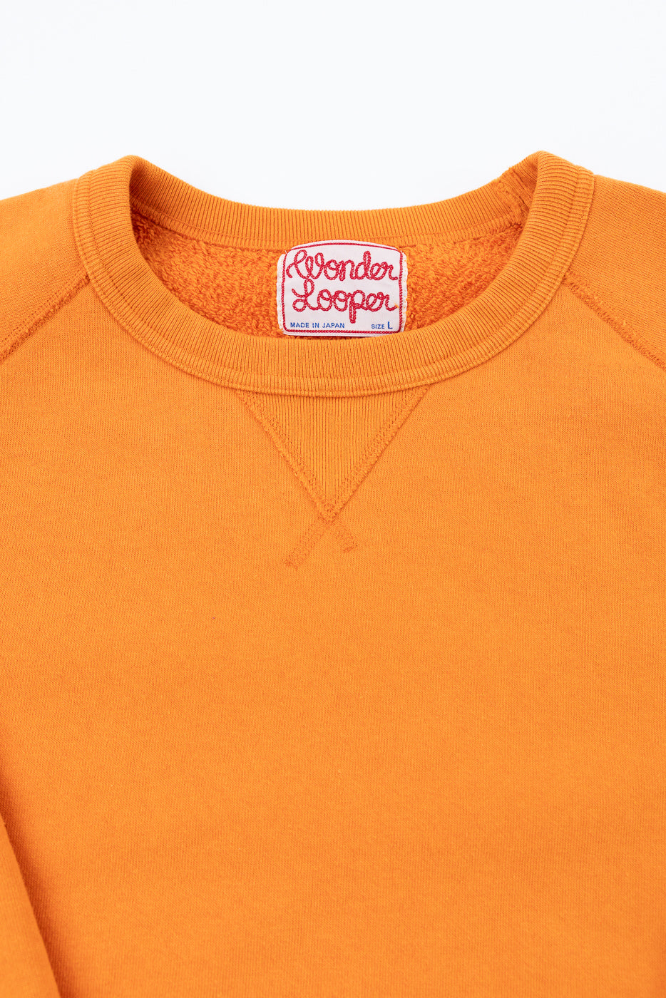 Close-up front view of orange crewneck sweatshirt showing Wonder Looper tag, ribbed collar, and V-stitch detail.