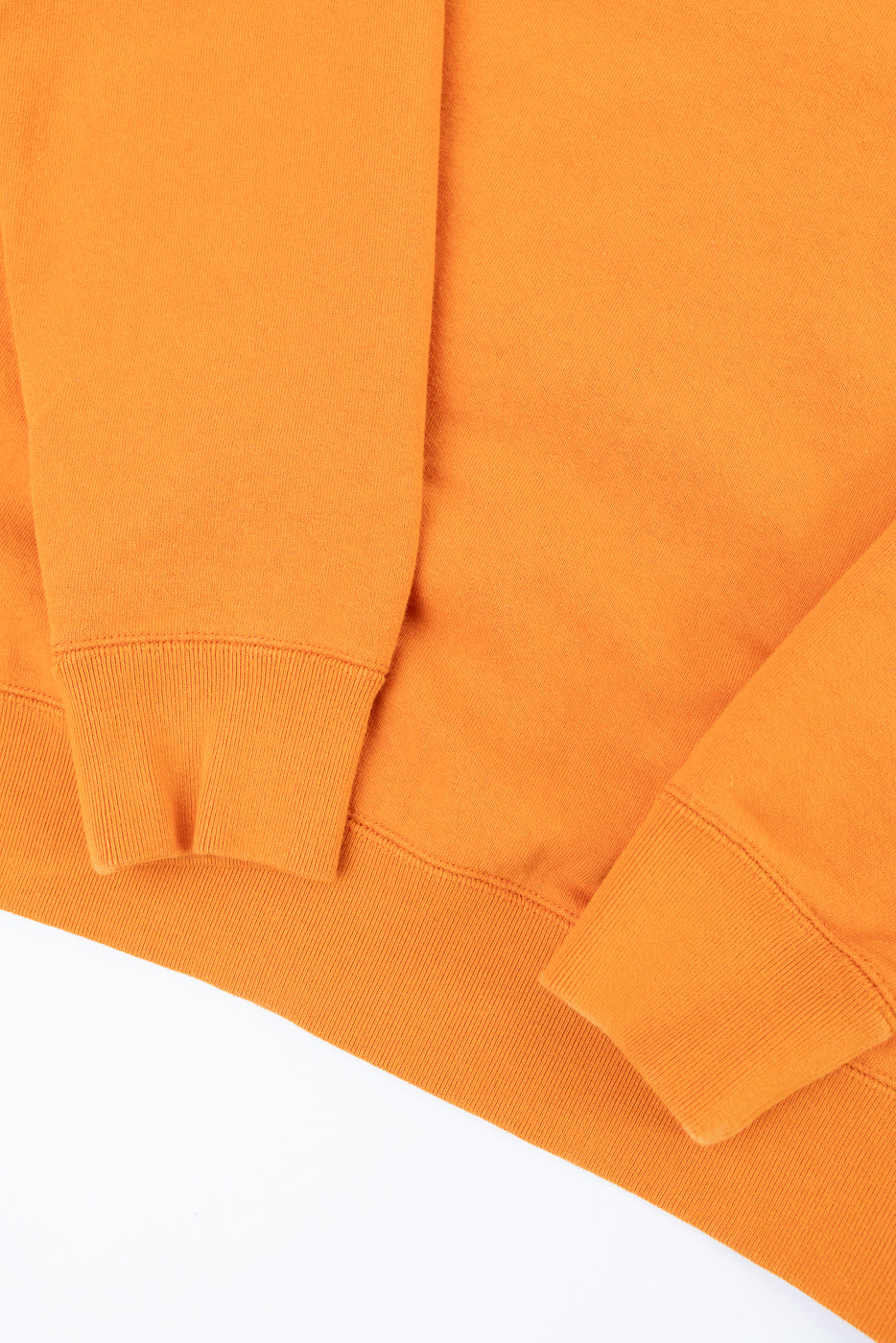 Close-up of orange crewneck sweatshirt front, showing ribbed cuffs and hem, soft cotton texture