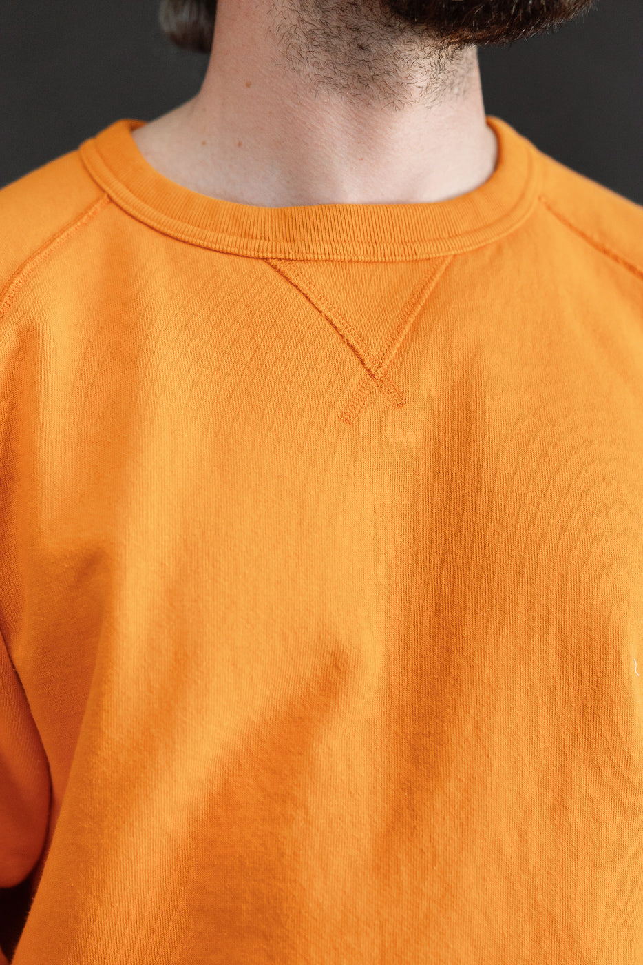 Close-up front view of orange crewneck sweatshirt, showcasing ribbed collar and shoulder seams on male model.