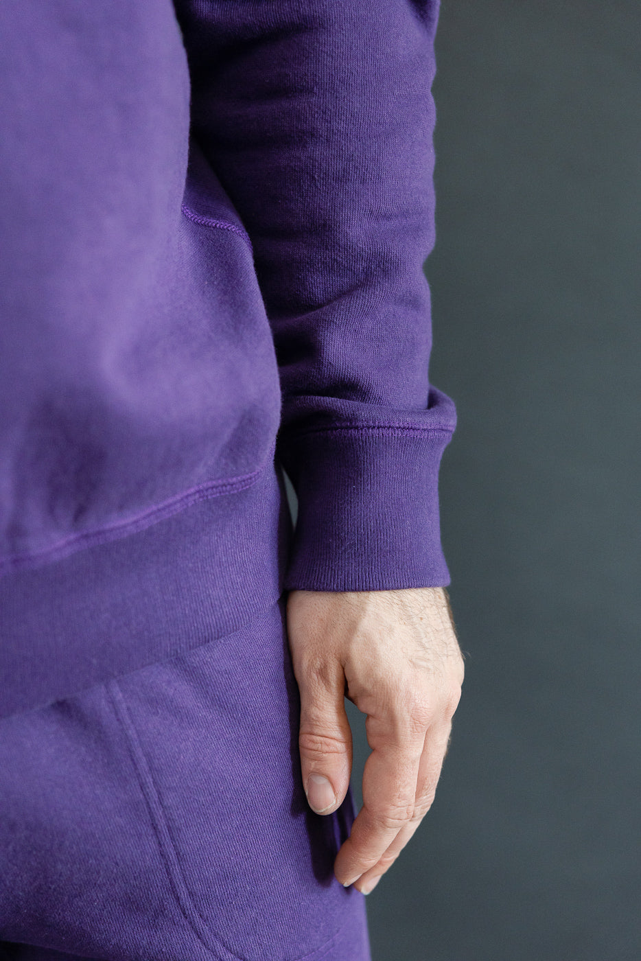 Close-up side view of male model's purple hoodie sleeve cuff, showing ribbed hem and fabric texture
