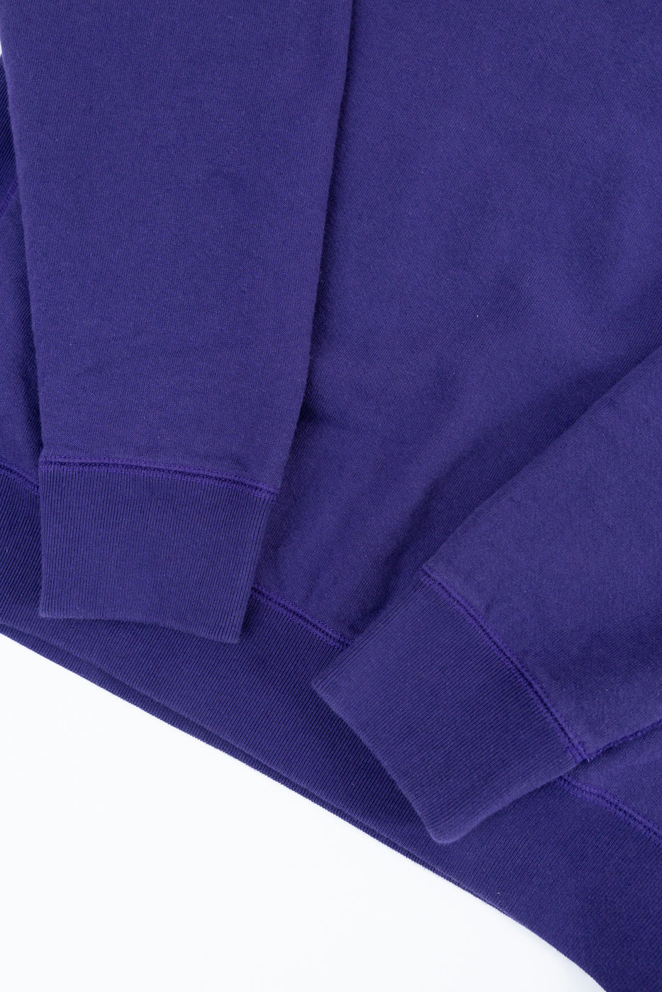 Close-up of purple sweatshirt's ribbed cuffs and hem, showcasing fabric texture and stitching details.