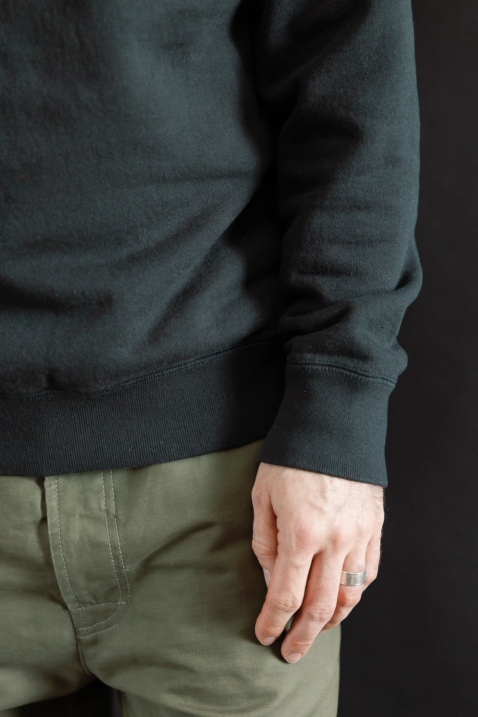 Pullover Crewneck - Super Looper French Terry - Sumi: Close-up of a hand wearing a dark sweatshirt, showcasing the textured Tsuriami knit fabric with ribbed details, embodying Dant's premium menswear craftsmanship.