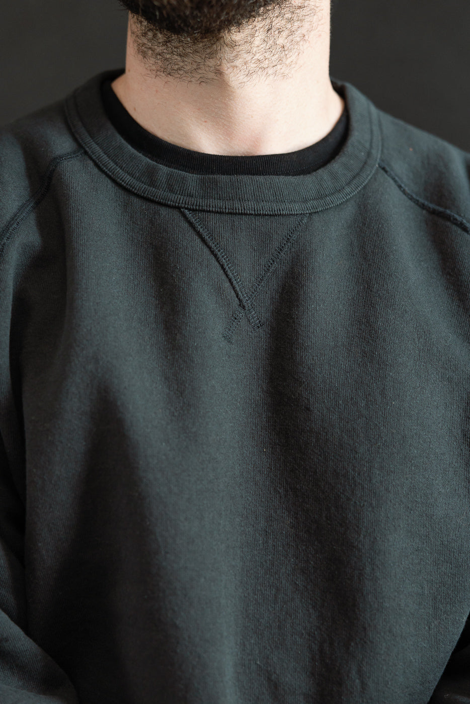 Close-up of a model wearing the Pullover Crewneck - Super Looper French Terry - Sumi, showcasing its textured French terry fabric and ribbed binder collar with vintage-style V-gusset.