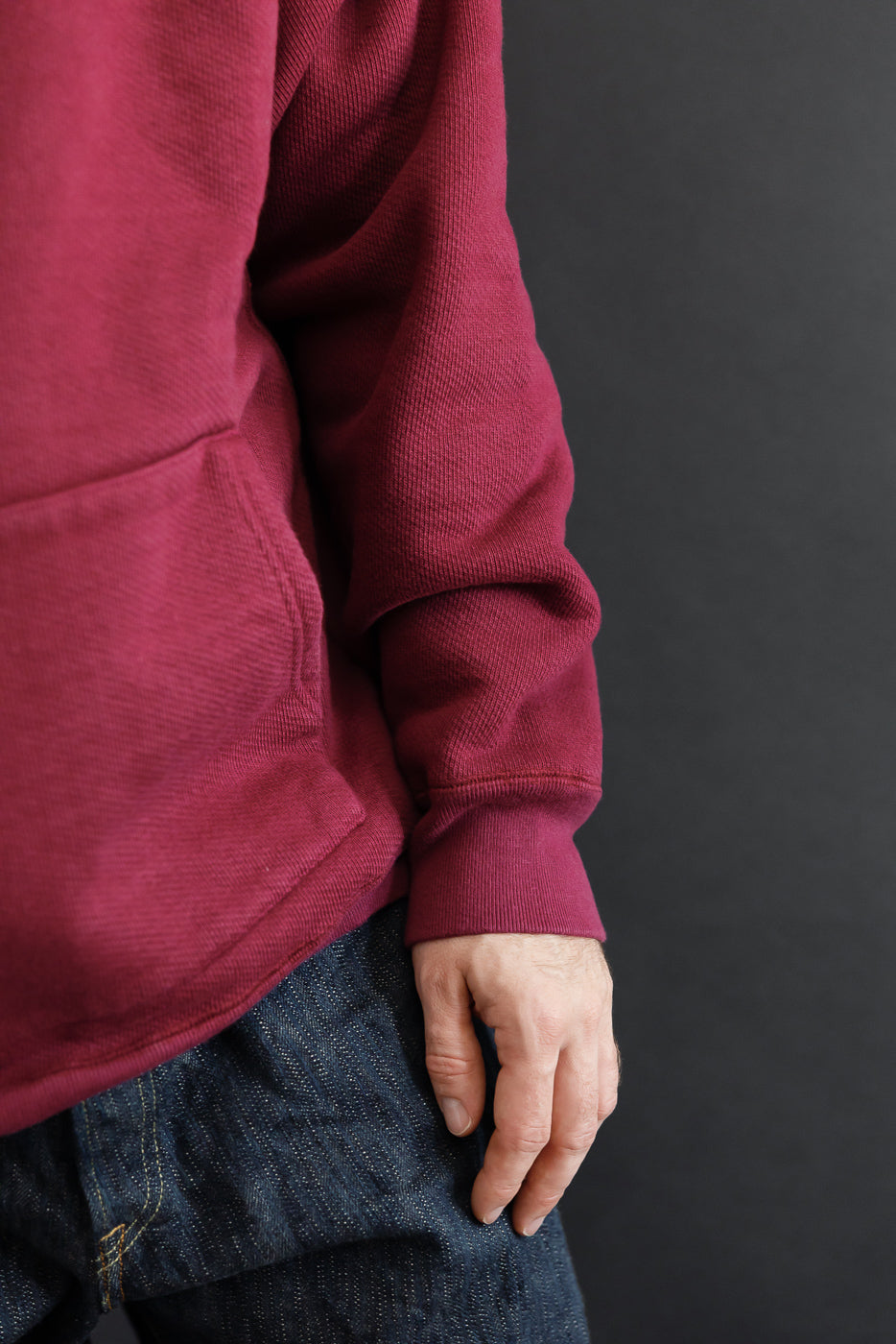 Side view close-up of a male model in a burgundy waffle-knit hoodie and dark selvedge denim.