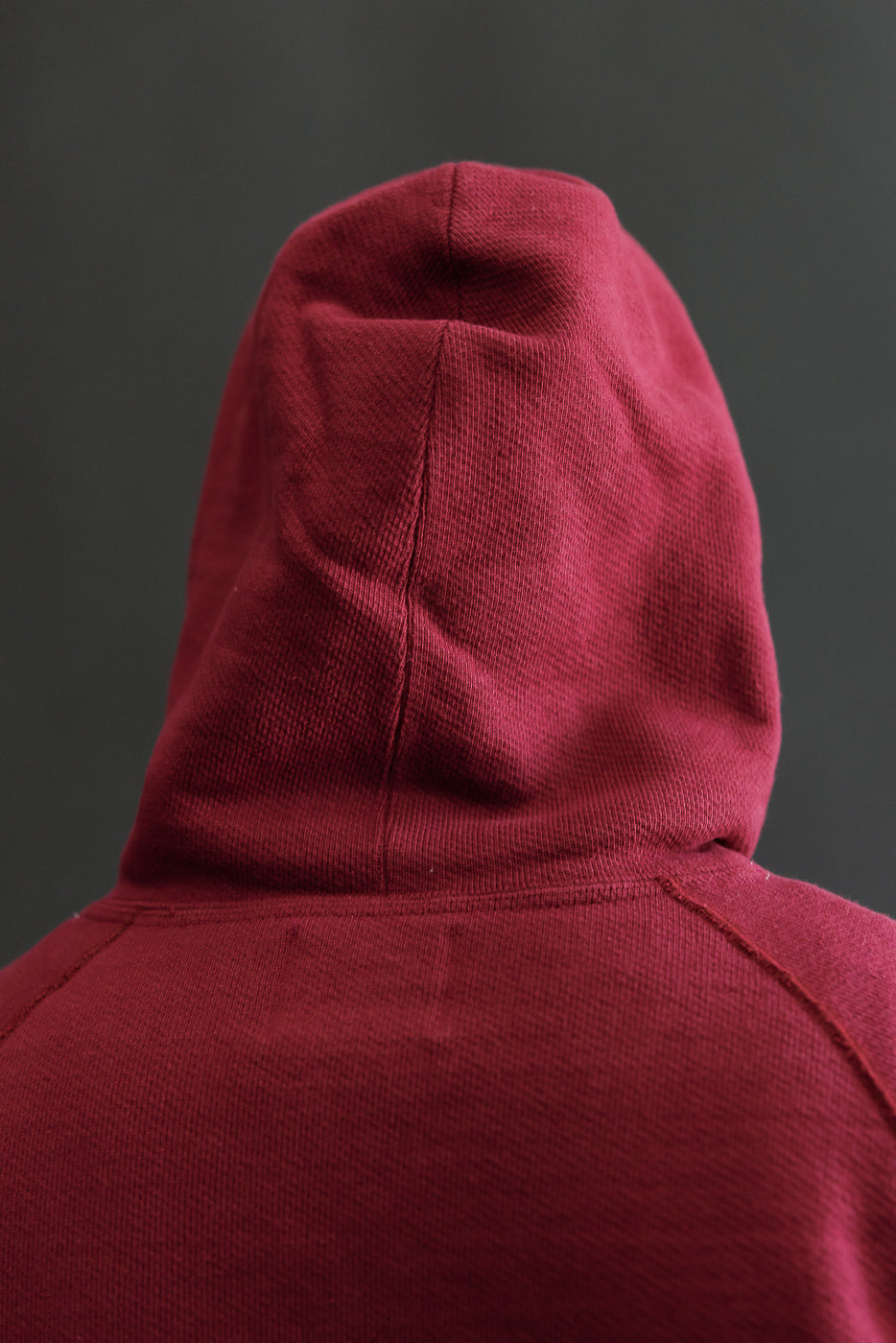 Close-up back view of a burgundy hoodie showing the textured knit fabric and hood.