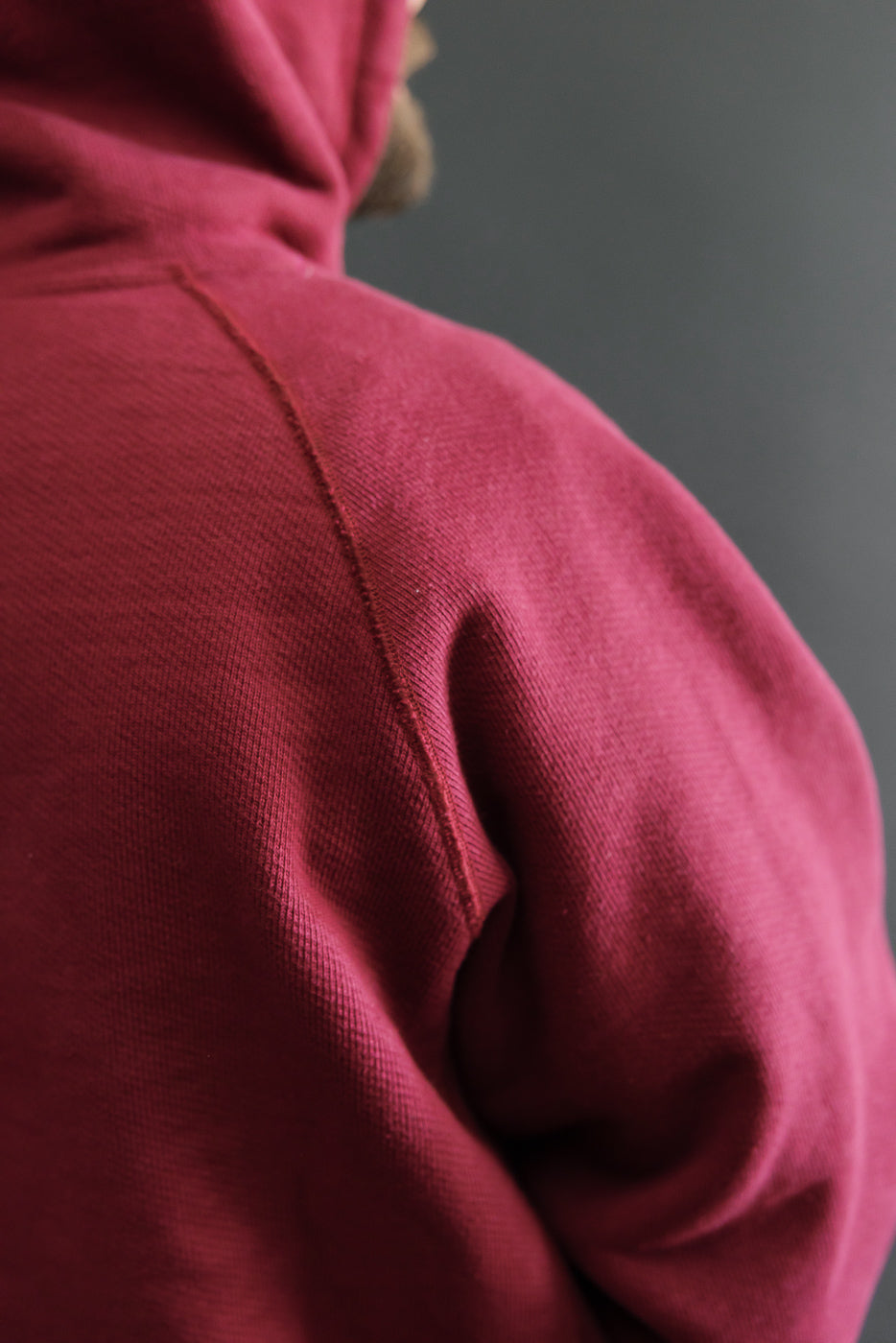 Close-up of the back shoulder and sleeve texture of a maroon hooded sweatshirt.