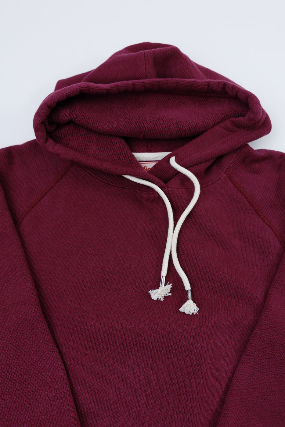 Close-up of the front collar and hood of a maroon hoodie with white drawstrings.