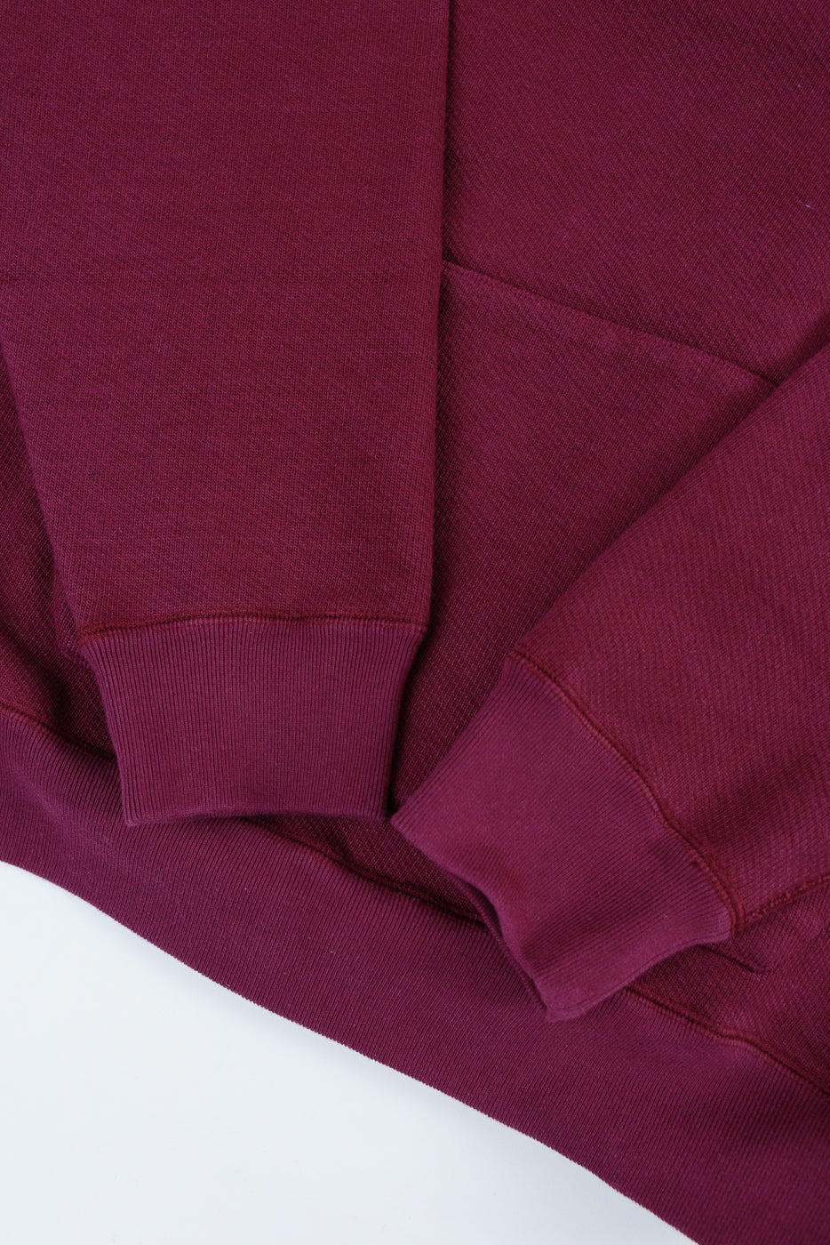 Close-up of a maroon sweatshirt's ribbed sleeve cuff and bottom hem, front view.