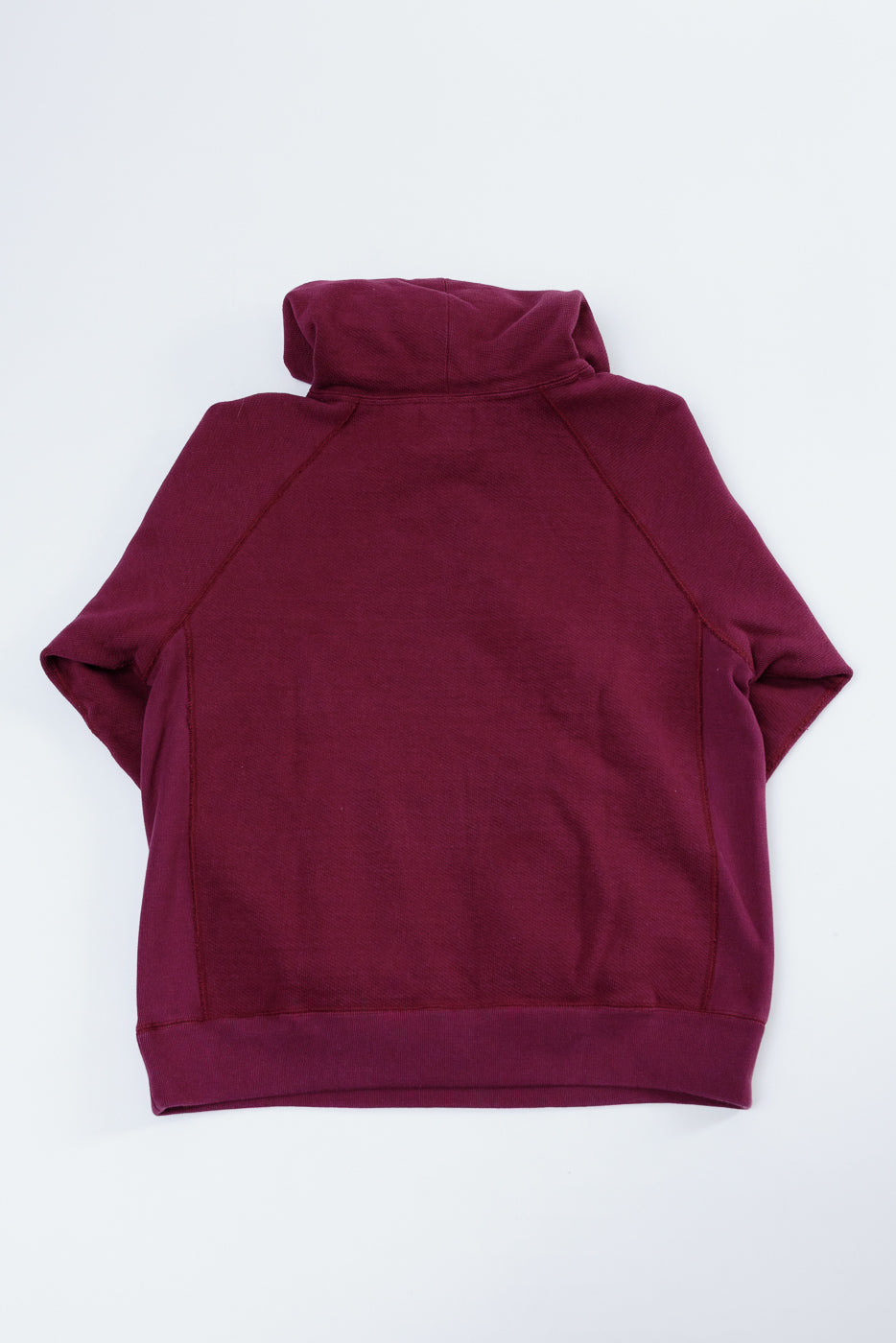 Back view flat lay of a burgundy hooded sweatshirt showing the raglan sleeves and hem.