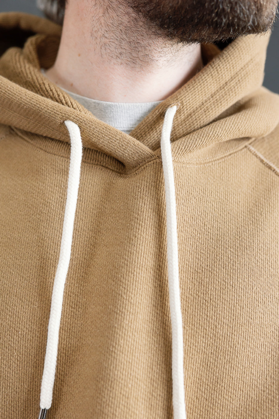 Close-up front view of Wonder Looper pullover hoodie in dune, double heavyweight French terry, showing hood, drawstrings, and fabric texture on male model, 5'9