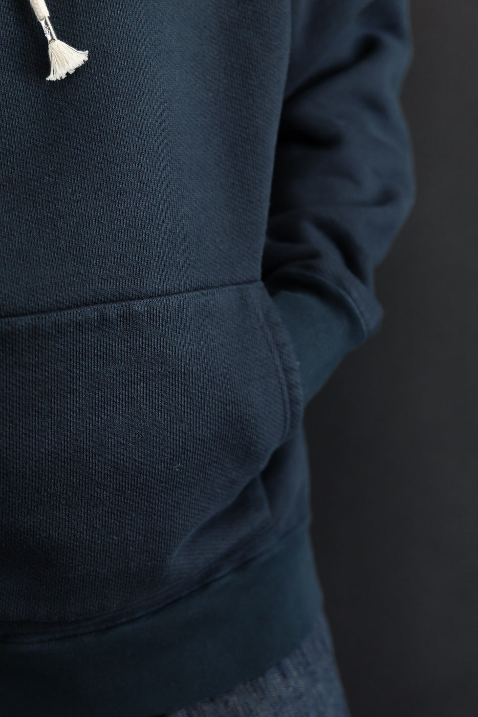 Close-up of the front left pocket and fabric texture of a navy hoodie on a male model.