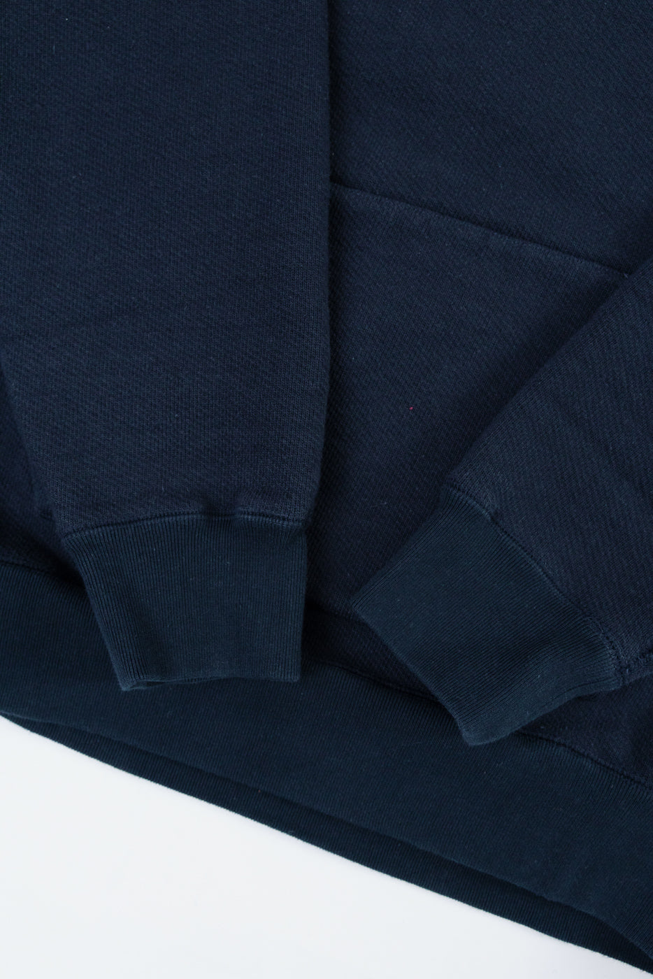Close-up of the ribbed cuffs and sleeve texture on a navy blue hoodie flat lay.