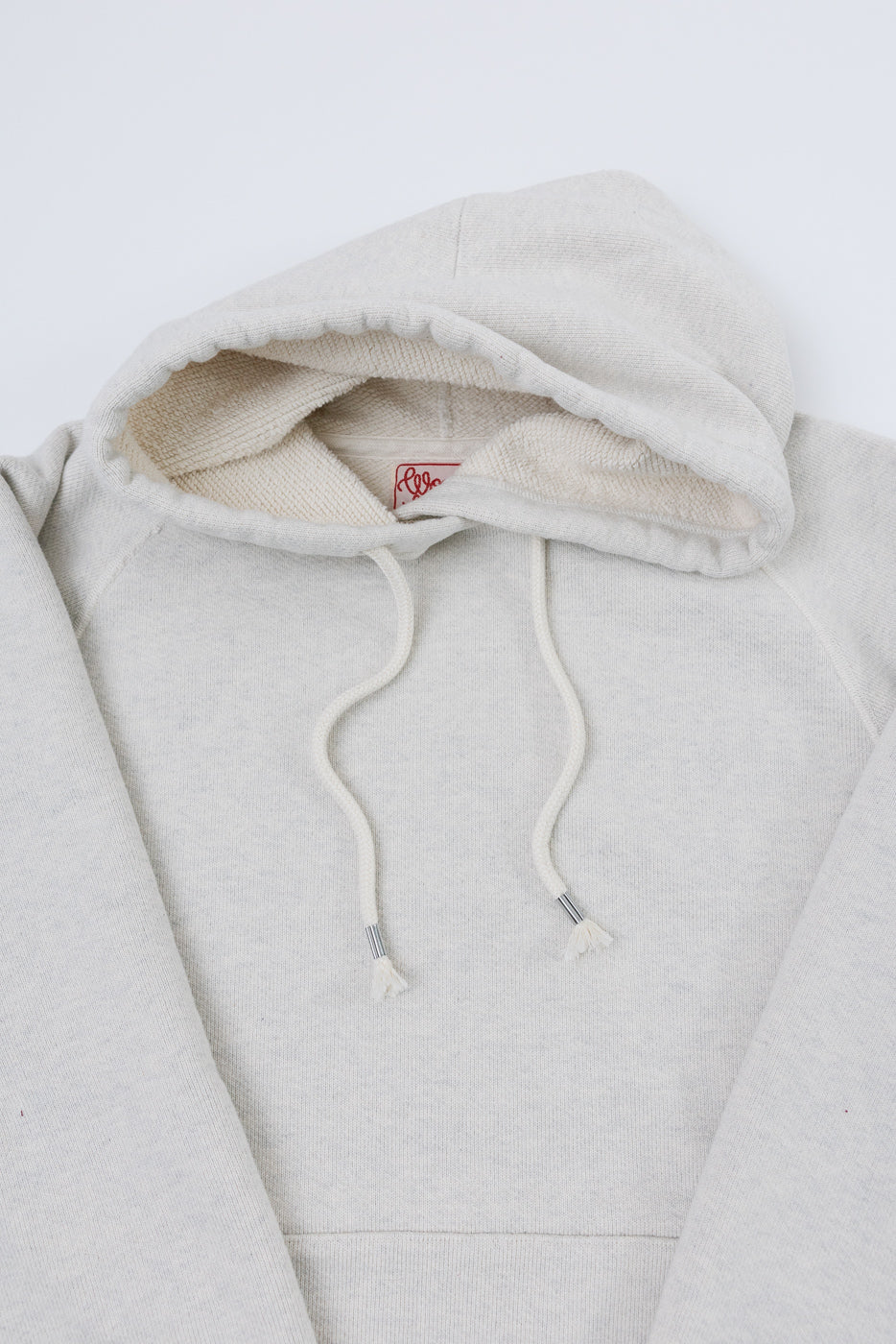 Close-up of the front hood and neckline of an off-white hoodie showing fabric texture and tag.