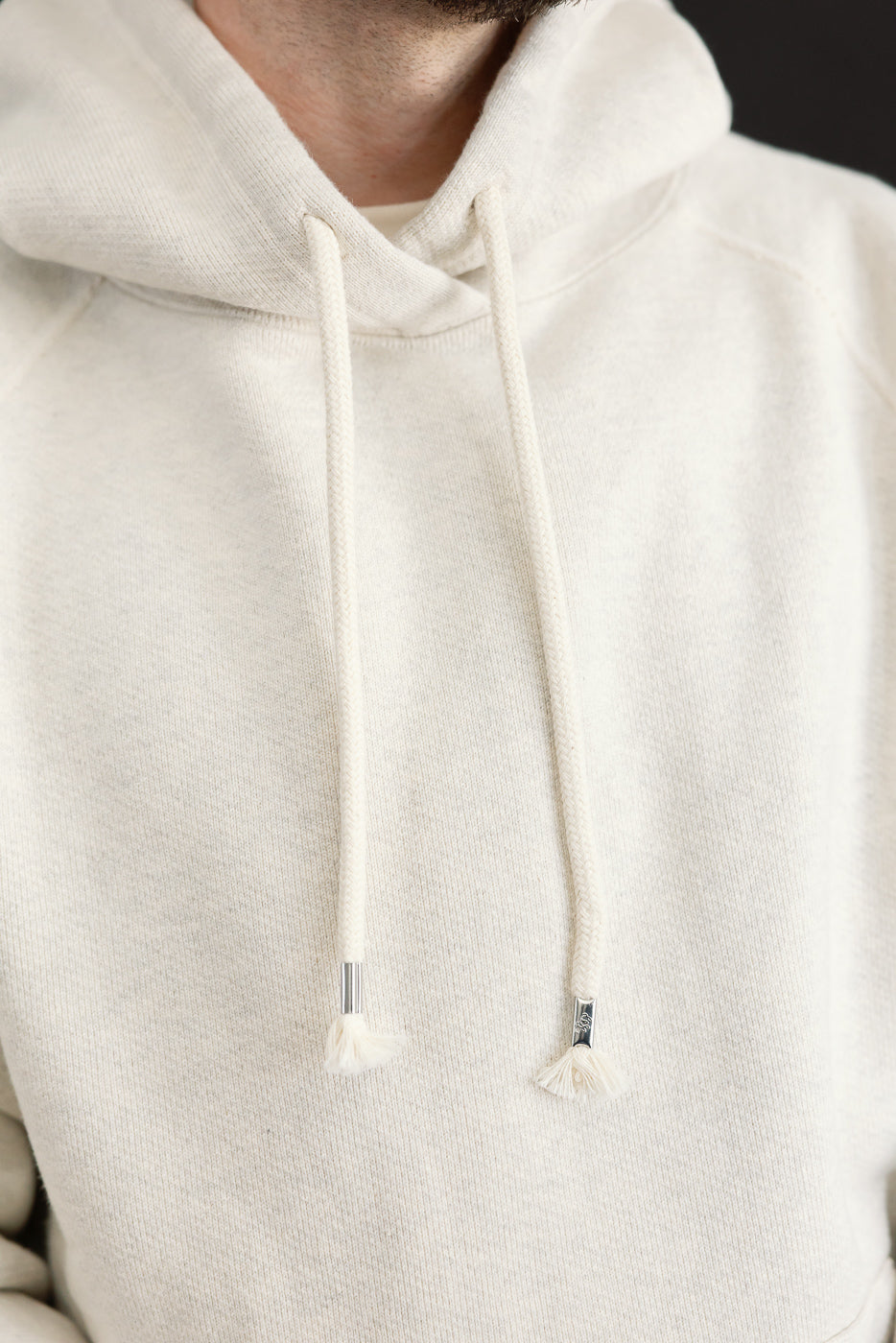 Close-up of the front neck and drawstrings of a white hoodie on a male model, 5'9