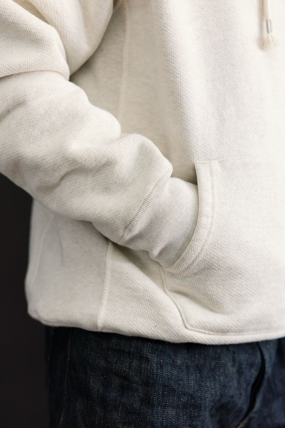 Close-up side view of a male model's cream hoodie pocket and textured fabric.