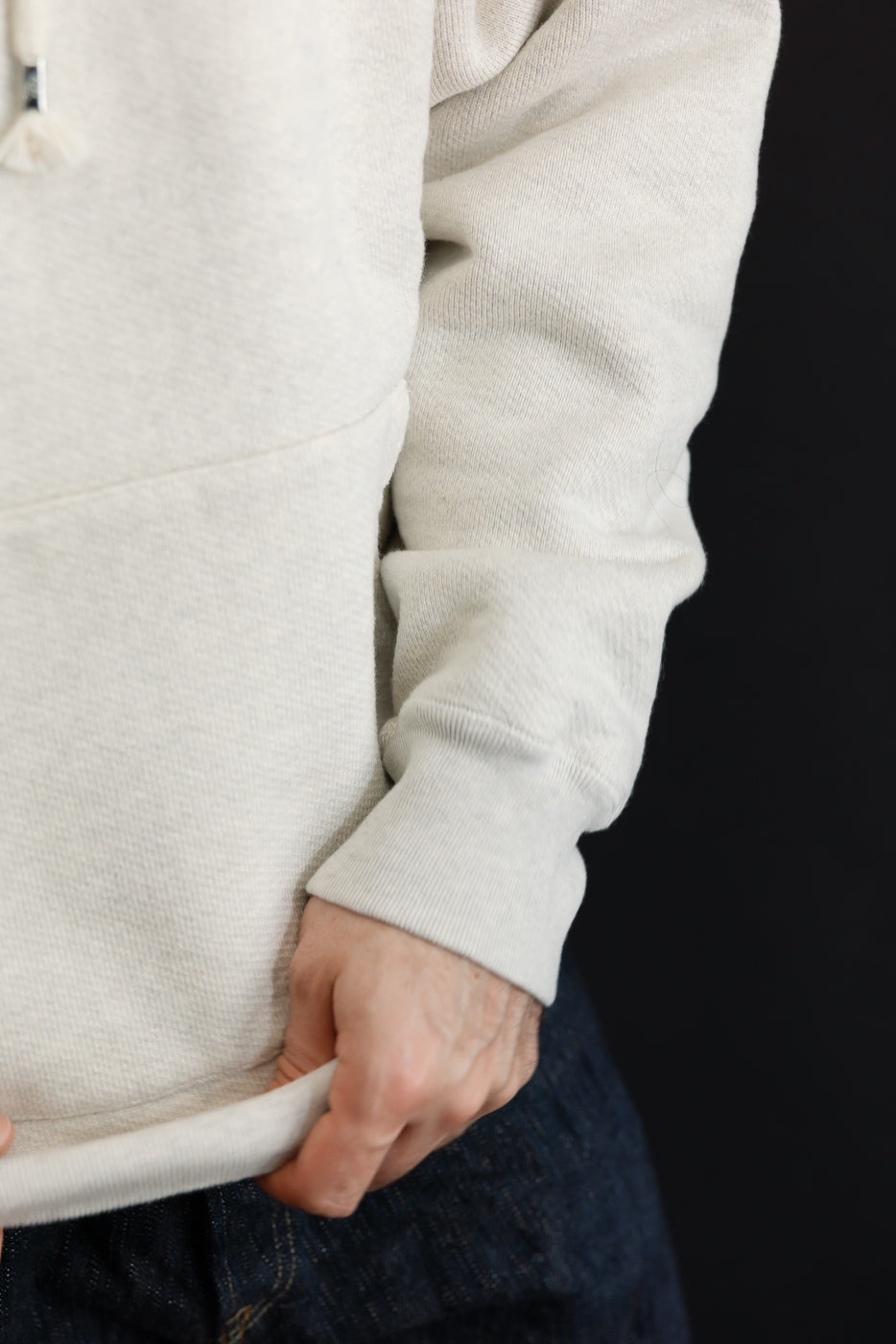 Close-up of the left side and ribbed cuff of a cream hoodie worn by a male model.