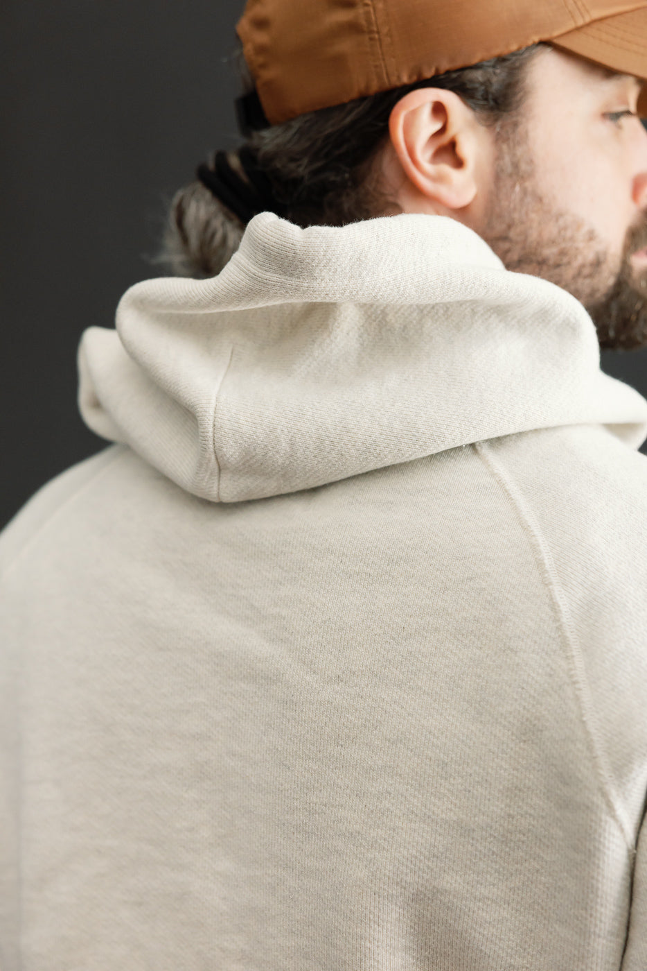 Close-up back view of a cream hoodie hood and shoulder fabric texture on a male model.