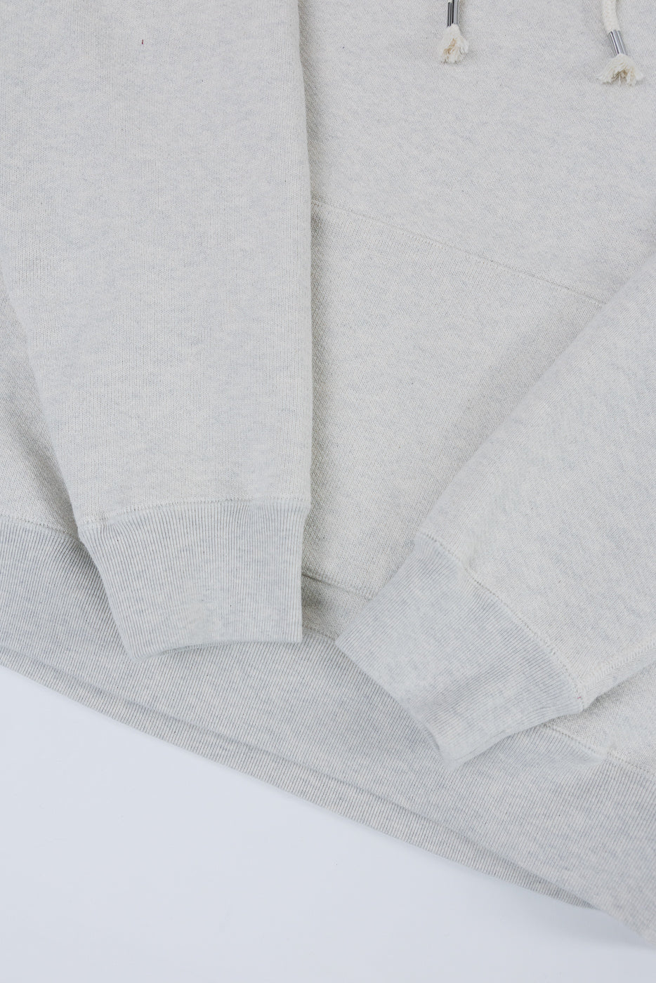 Close-up of the front bottom hem and ribbed cuffs of a light grey hoodie.