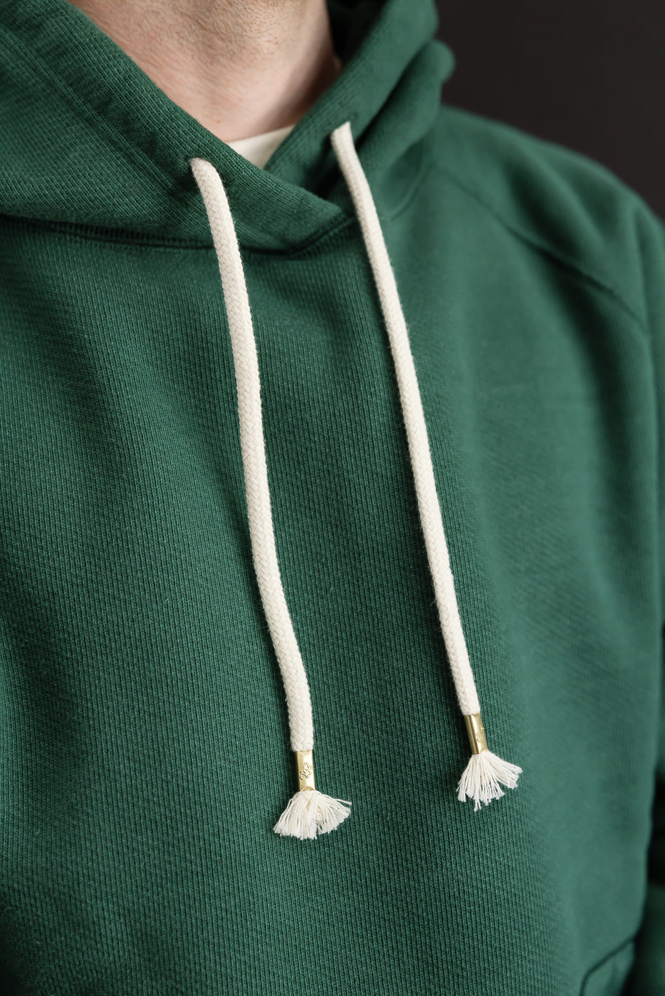 Close-up front view of a green hoodie's hood and drawstrings on a 5'9