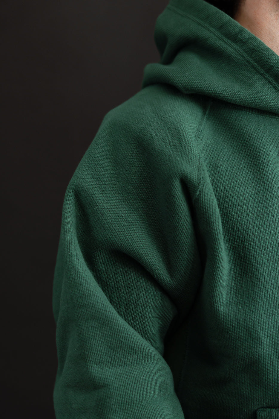 Close-up of the side and shoulder of a green waffle-knit hoodie showing fabric texture.