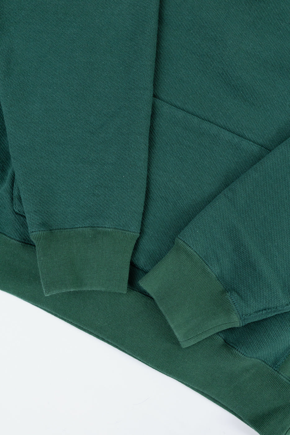Close-up of a green sweatshirt's front, showing ribbed cuffs and textured fabric.