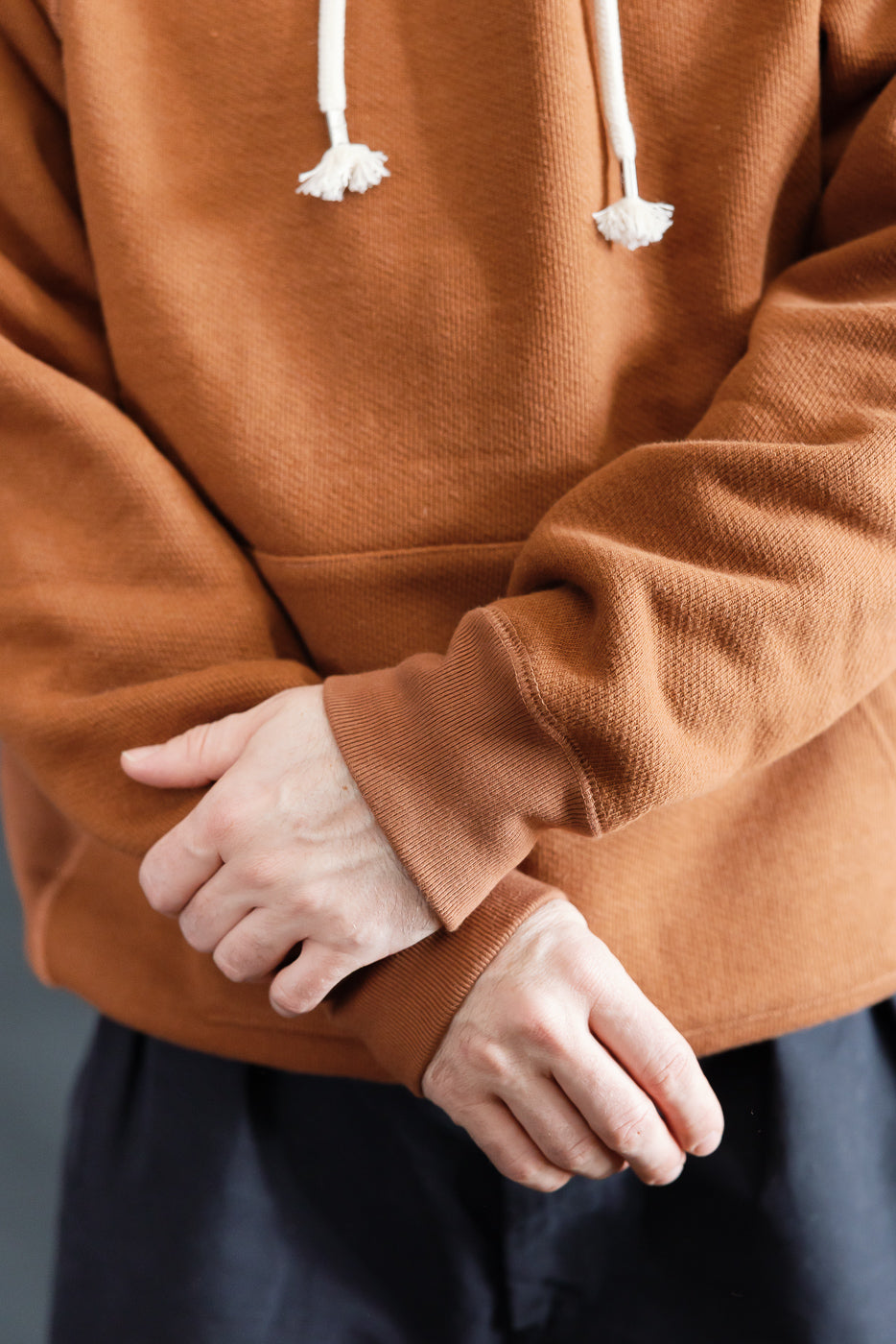 Close-up front of Wonder Looper pullover hoodie in rust French terry on male model, showing cuff, kangaroo pocket, and drawstrings; model is 5'9
