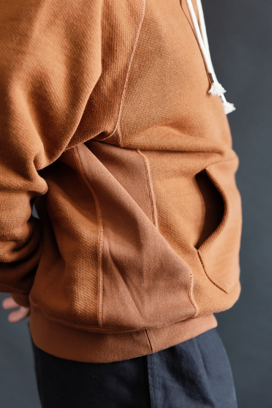 Close-up of male model wearing rust Wonder Looper pullover hoodie, left side pocket detail, heavyweight French terry.
