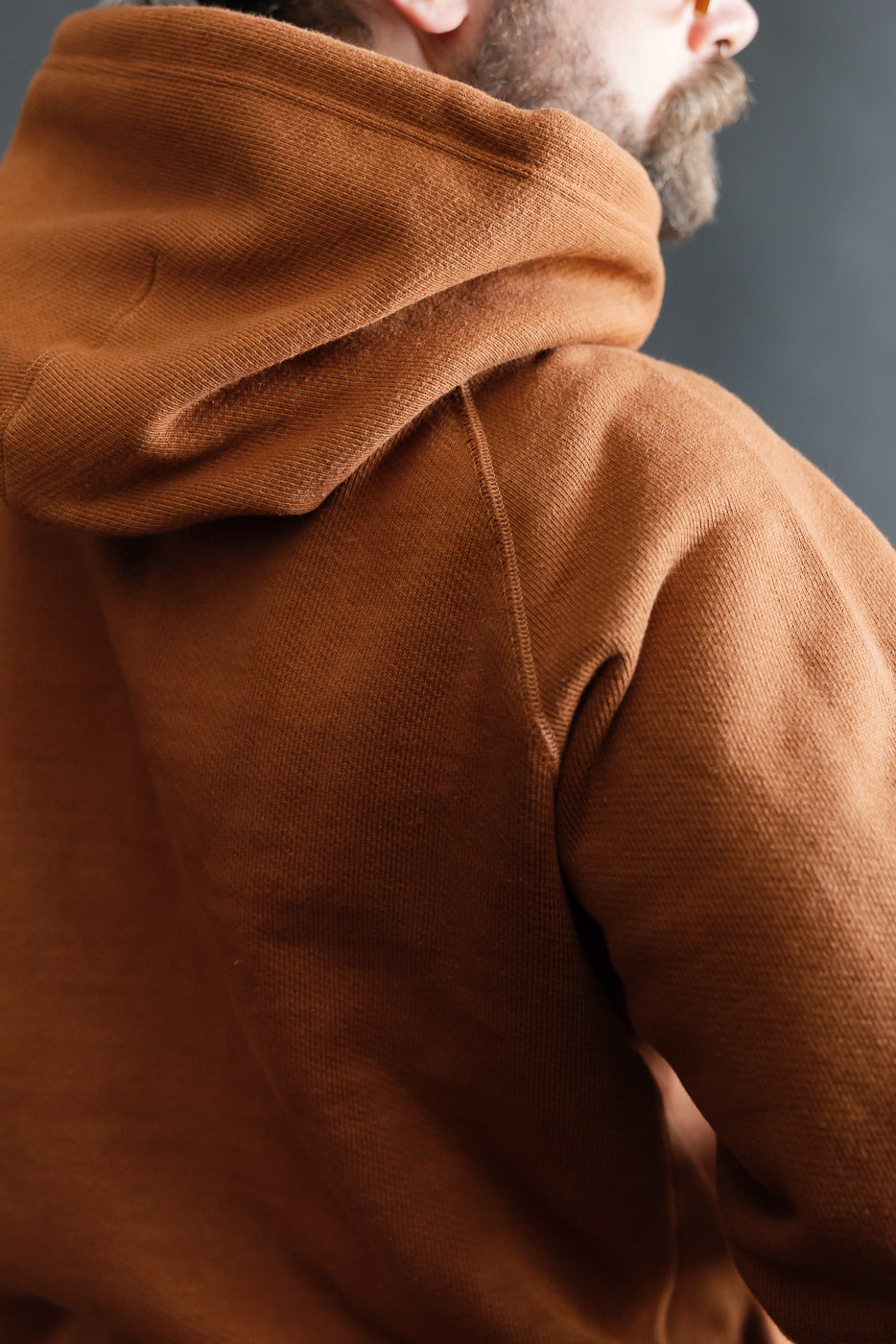 Close-up of back and hood details on rust Wonder Looper heavyweight French terry hoodie, worn by male model, 5'9