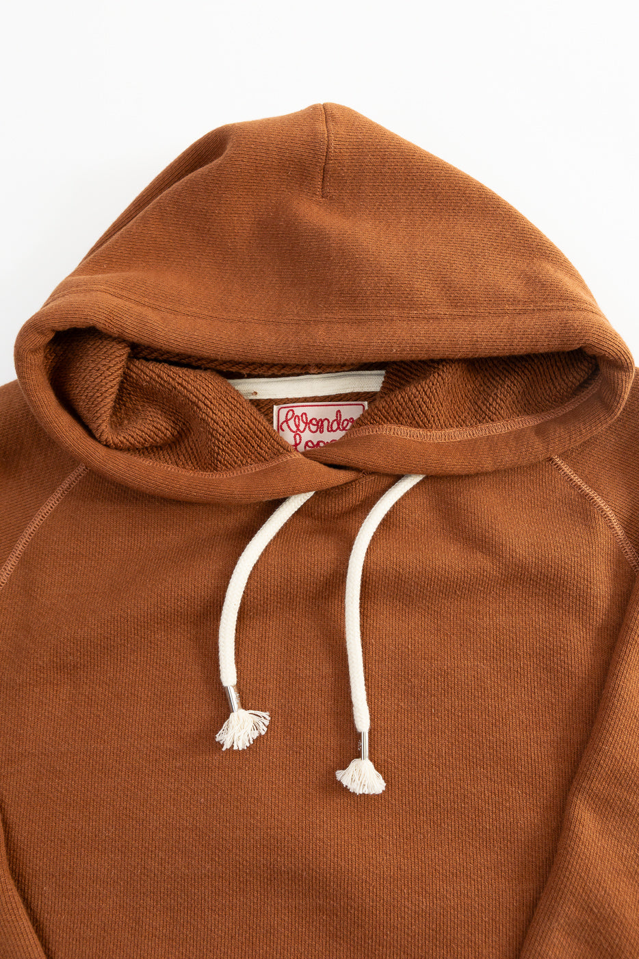 Close-up front detail of rust French terry pullover hoodie, drawstrings and fabric texture visible.