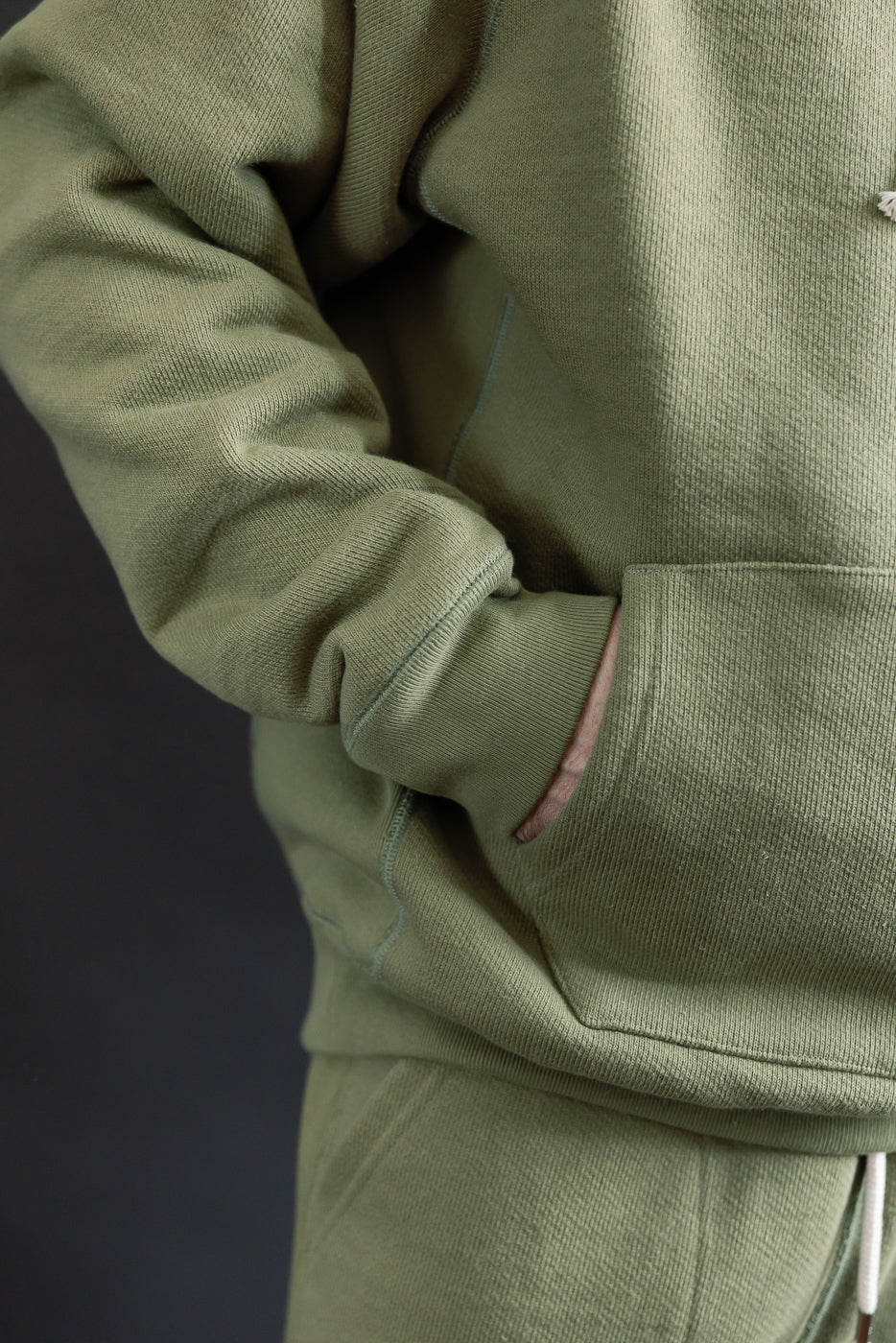 Close-up of front pocket and sleeve detail, sage green heavyweight French terry hoodie on male model