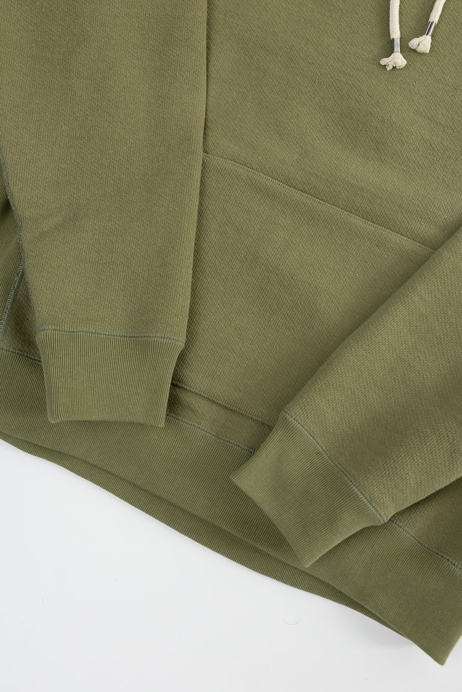 Close-up of sage green French terry pullover hoodie front, highlighting cuff, hem, pocket, and drawstring details